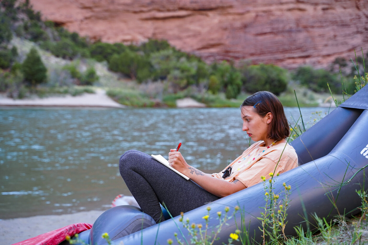 Girl sits in the kayak while journaling on the beach in a Gates of Lodore Rafting trip - Mild to Wild