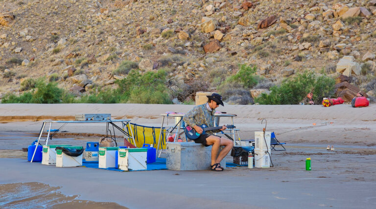 Man playing guitar in the camp kitchen on a Cataract Canyon rafting trip 