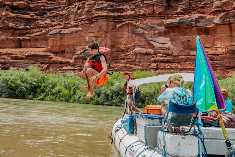 Kid doing a canon ball off a raft into the Colorado River in Cataract Canyon